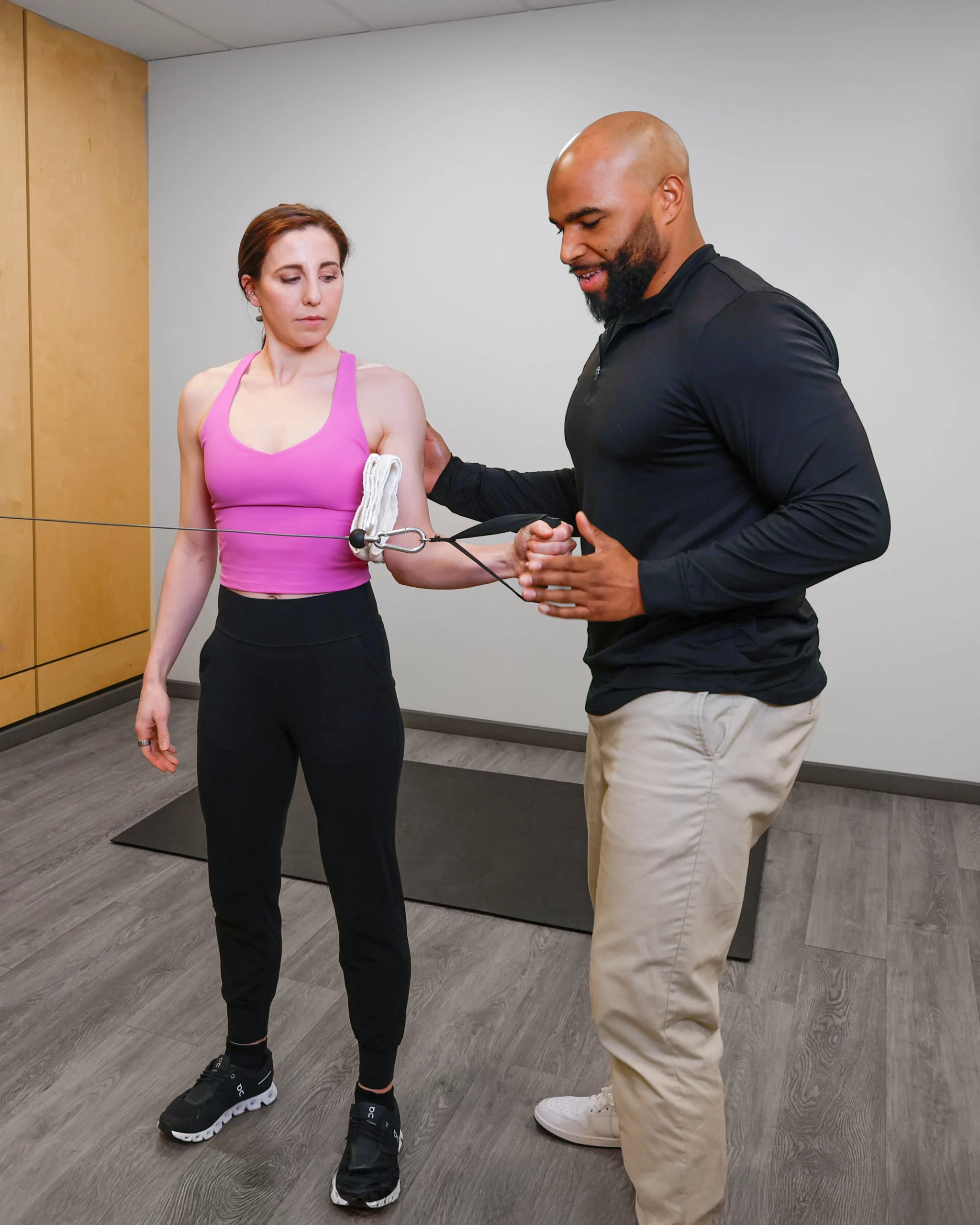 Physiotherapist guiding a female athlete through resistance band shoulder rehabilitation exercise in a sports physiotherapy clinic.