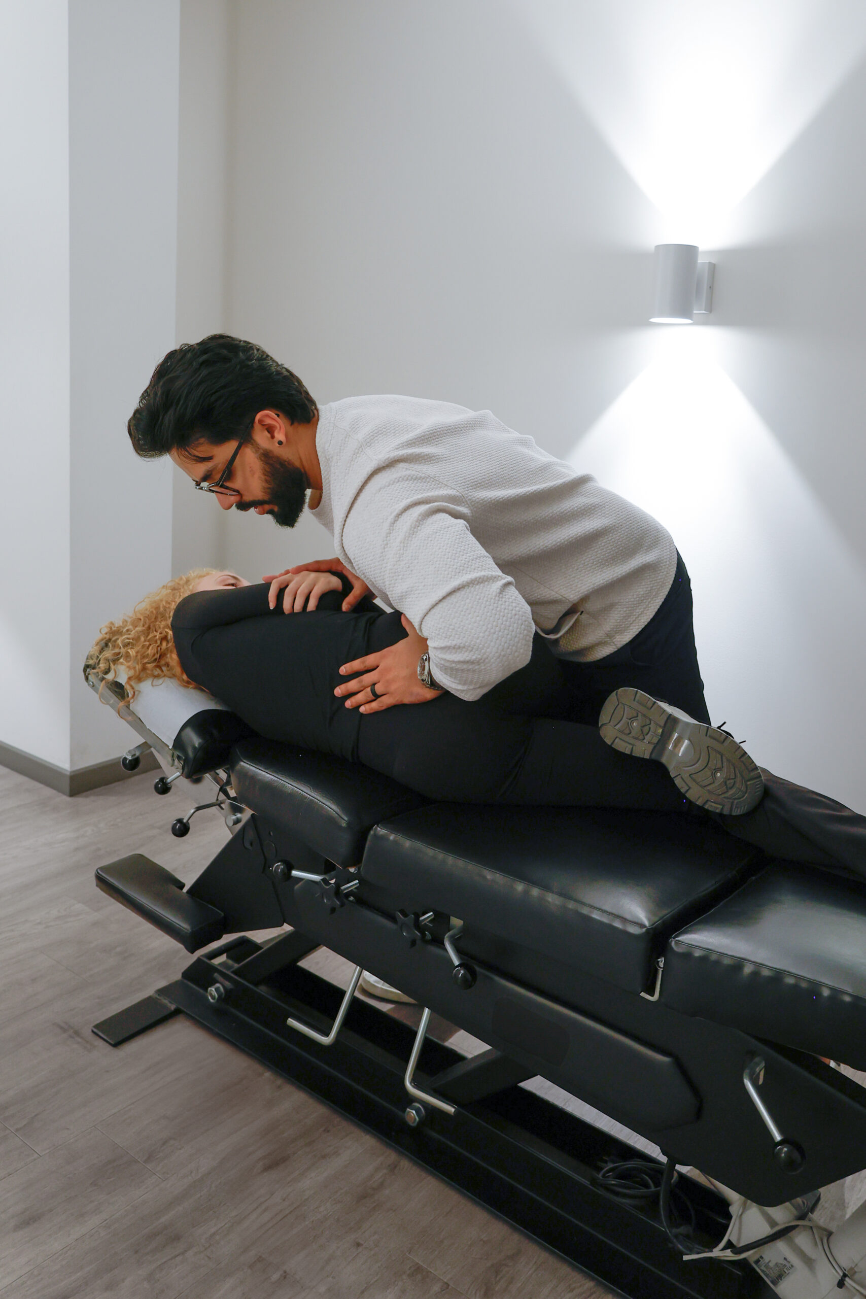 Chiropractor performing a back adjustment on a patient lying on a chiropractic table in a clean treatment room.